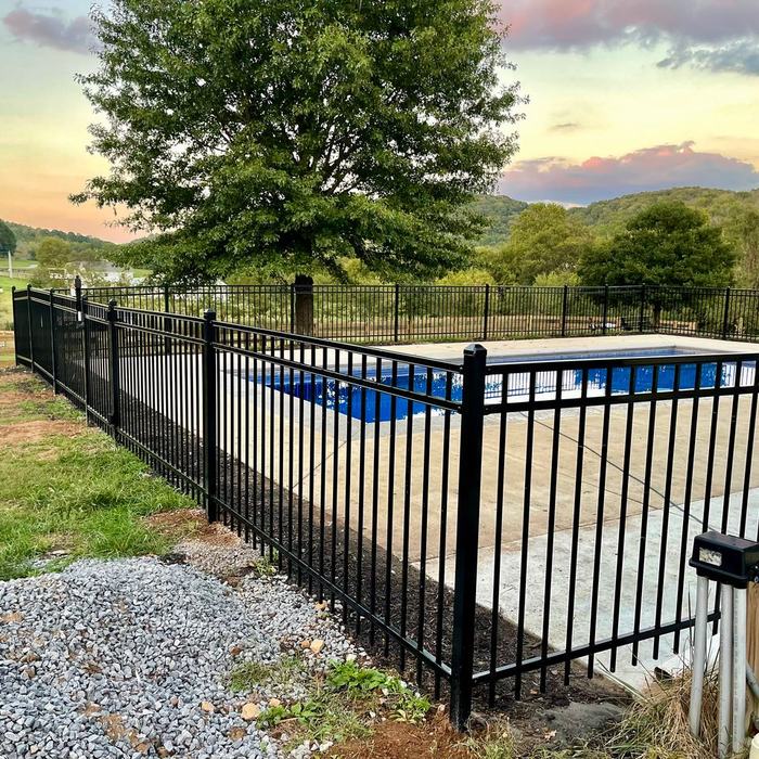 Black ornamental aluminum pool fence at sunset with a swimming pool behind it