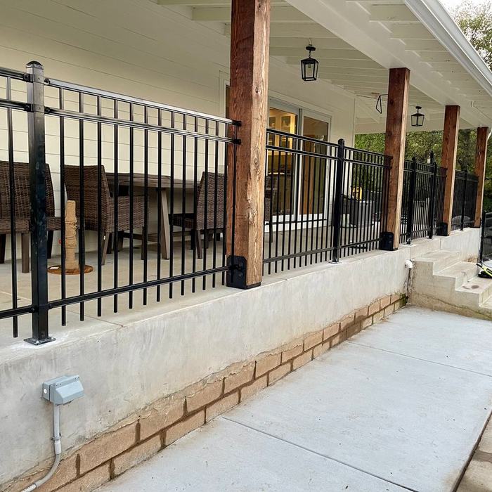 Black metal porch railing installed along a covered patio and retaining wall