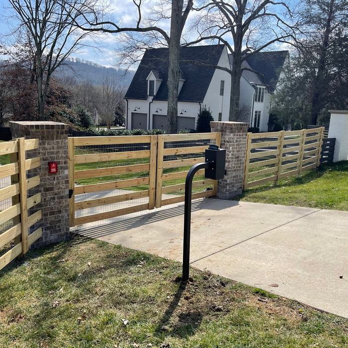 Horizontal rail fence and brick columns across the front of a newly built home