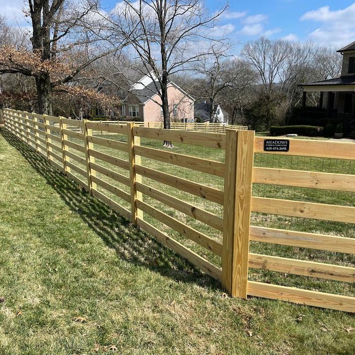 Four board rail fence with a matching gate along the edge of a subdivision lot