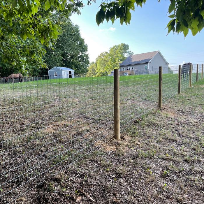 Woven wire livestock fence with wood line posts across a freshly worked pasture