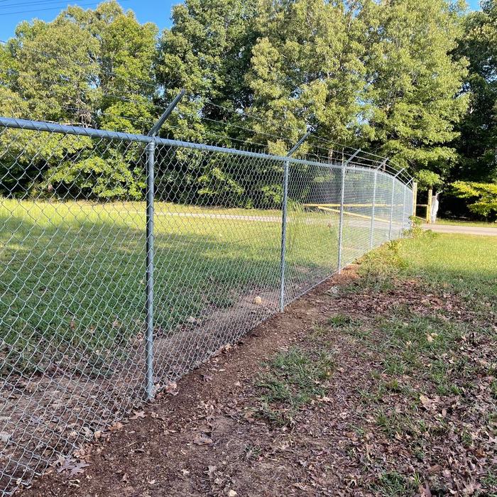 Chain link fence corner post set at the edge of a wooded lot