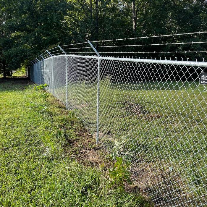 Galvanized chain link fence with a curved top rail running along a grassy bank