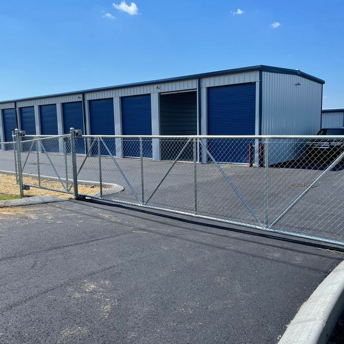 Chain link entry gate standing open in front of blue roll up doors