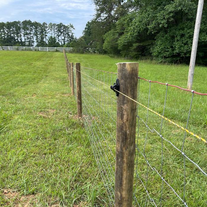 High tensile livestock wire with electric line on wood posts in a hay field