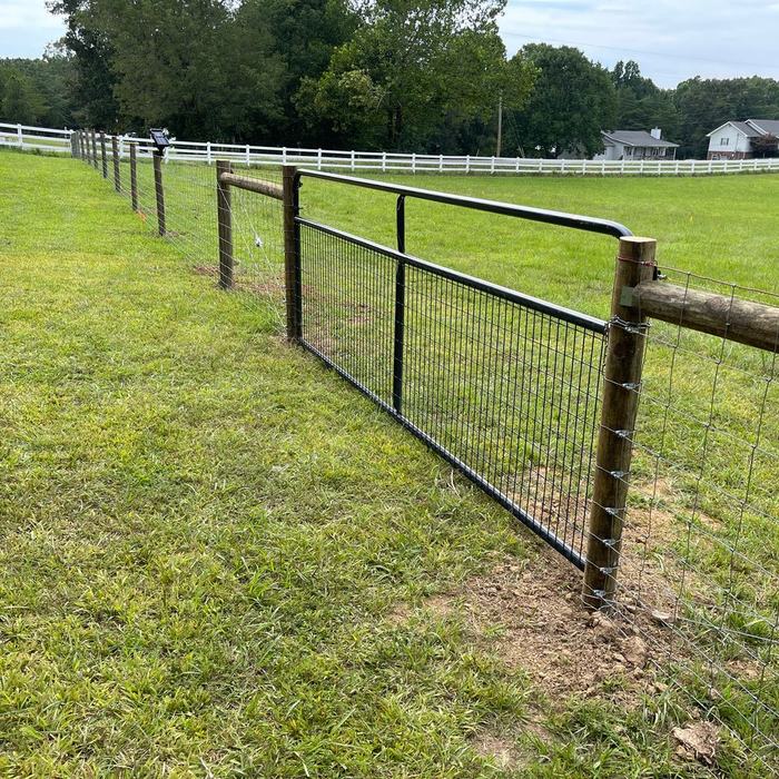 Wood post livestock fence with a black metal farm gate and white board fence beyond