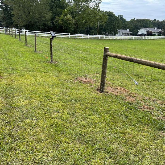 Woven wire livestock fence running downhill toward a neighborhood