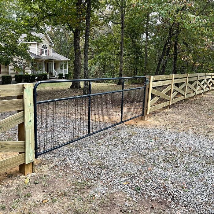 Rail fence with a black metal drive gate at a wooded country property